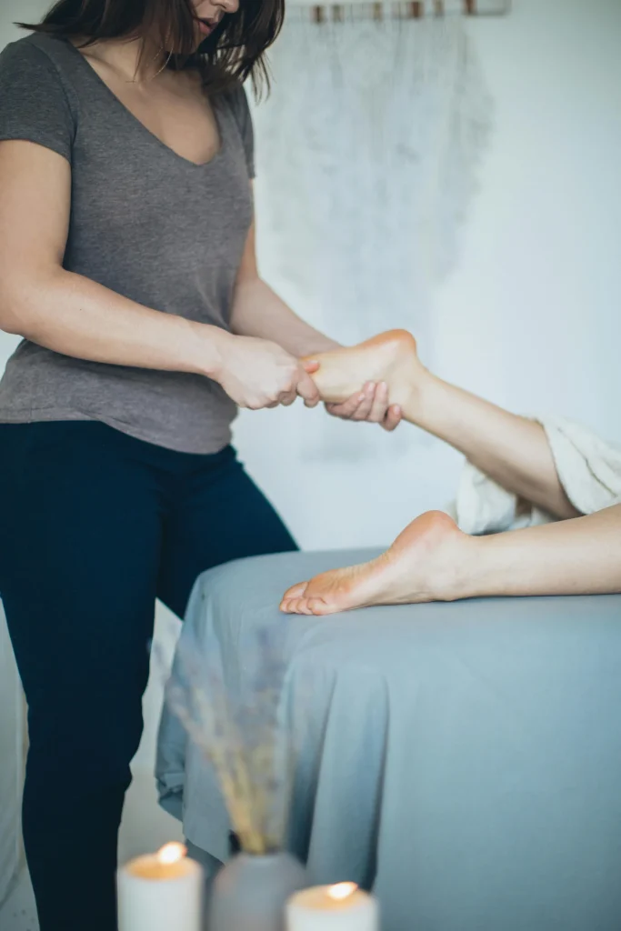 Dor no calcanhar ao acordar: o que costuma estar por trás (e o que ajuda) Uma mulher realiza uma sessão de reflexologia podal em um cliente deitado em uma maca.