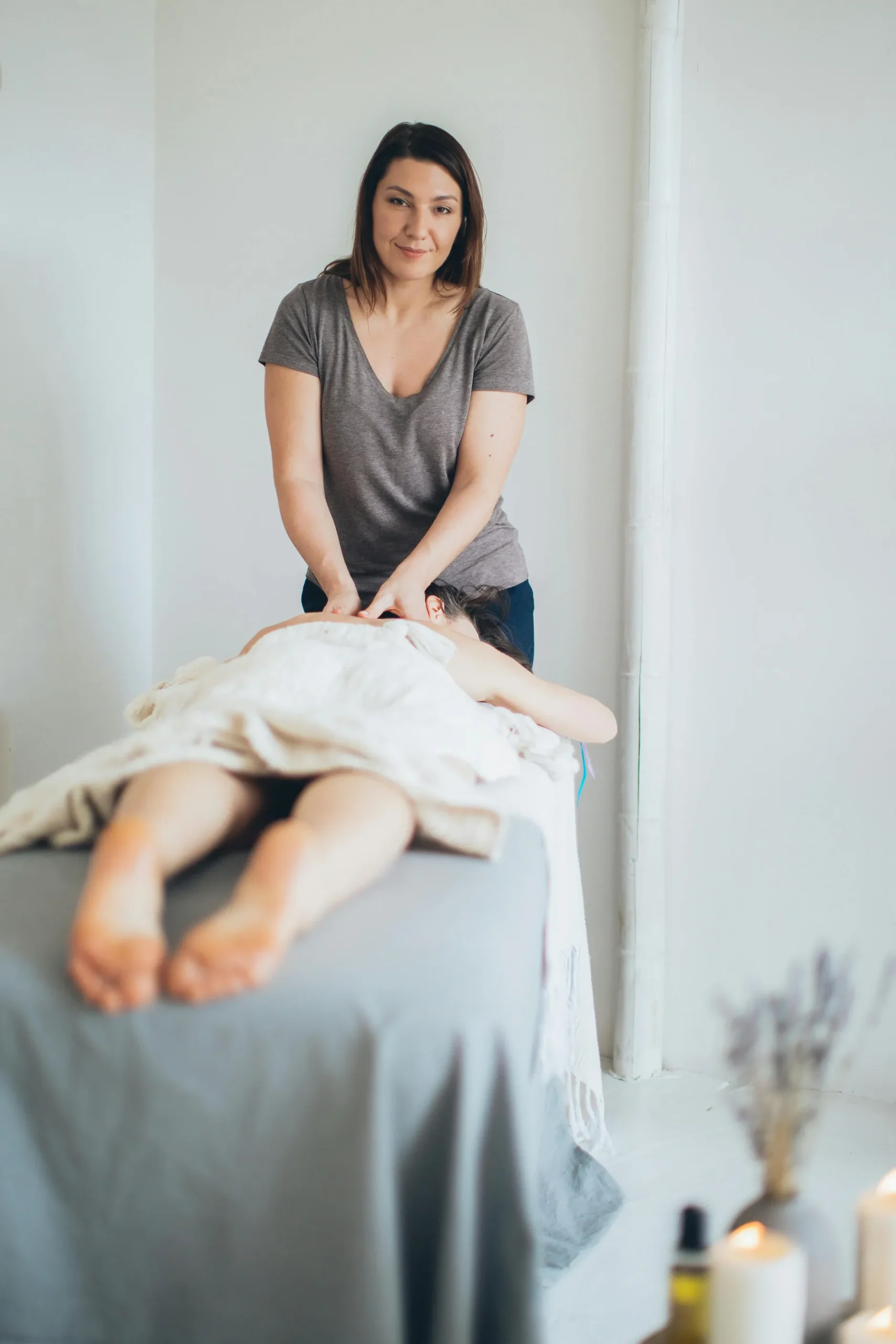 Uma massoterapeuta realiza um tratamento de massagem em uma pessoa deitada em uma maca.