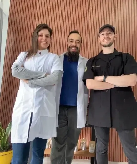 Conheça a Equipe de Especialistas em Massoterapia do Espaço Tao Foto de três profissionais de massoterapia posando juntos em frente a uma parede de madeira.